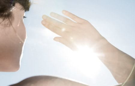 Mulher com a mão na frente do rosto para se proteger do sol