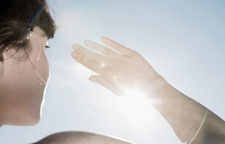Mulher protegendo os olhos do sol com a mão direita.