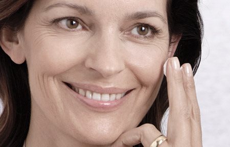 Mulher aplicando creme sobre a face.