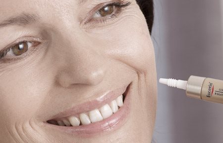 Mulher aplicando produto Eucerin na bocheca esquerda.