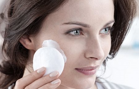 Mulher aplicando creme na face com algodão