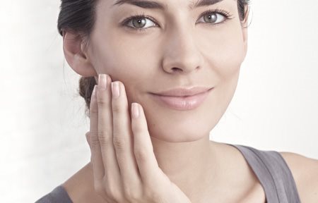 Mulher aplicando creme sobre a face.