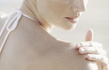 Mulher aplicando creme no ombro direito.